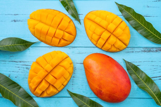 Mango - Fresh chopped tropical mango fruit isolated on bright vibrant light blue wooden table background, top view, flat lay layout, overhead shot.