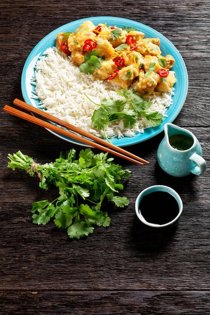 Mango glazed spicy chicken breast chunks with rice on a blue plate with chopsticks on a dark wooden table vertical view from above