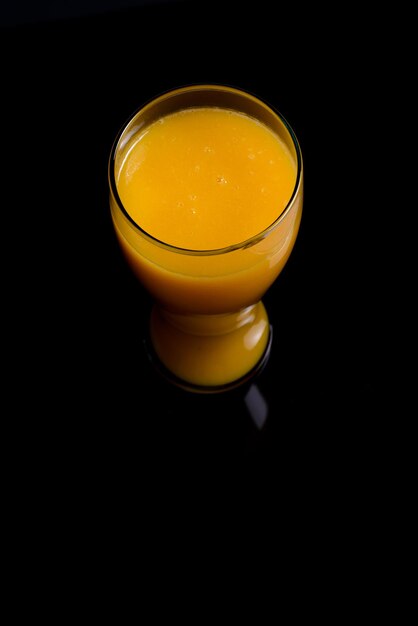 Mango juice glass and group of mangoes on black glass table. Blue background. Top view.