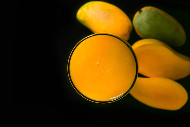 Mango juice glass and group of mangoes on black glass table. Top view.