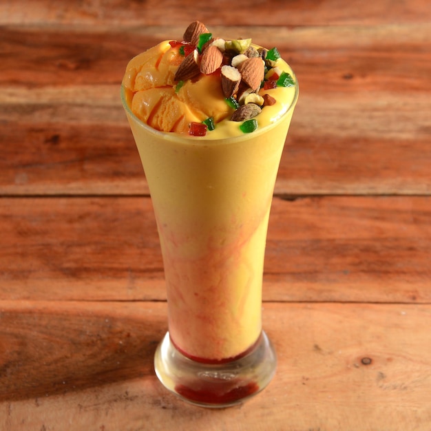 Mango Mastani indian street food mango juice and ice cream blended and topped with dry fruits and nutsserved in a glass over a rustic wooden background selective focus on top