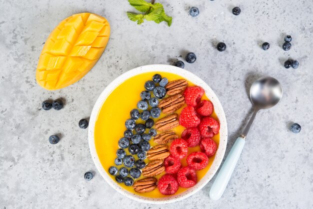 Mango and orange smoothie bowl with fresh berries and nuts.