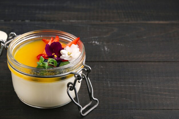 Mango panna cotta with flower and mint close up on wooden table.