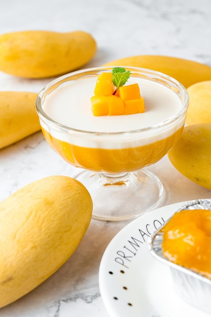 Mango pudding topping met verse rijpe mango gesneden dobbelstenen vorm en munt in glazen kom op een marmeren tafel cake in café of bakkerij winkel