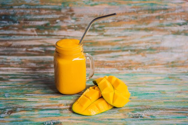 Mango-smoothie en stalen rietje op een geschilderde houten ondergrond