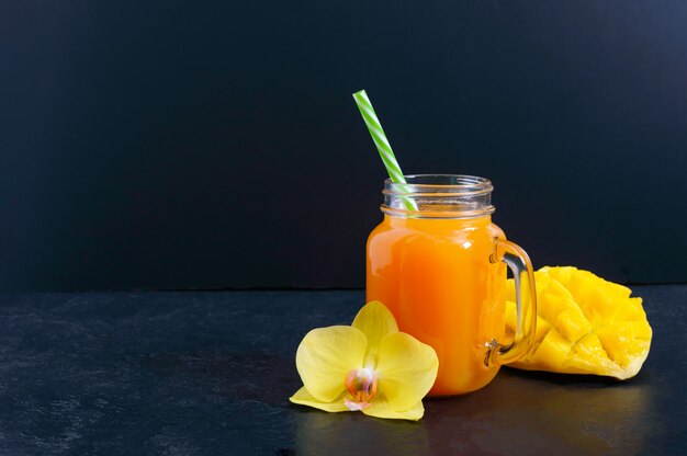 Mango smoothie in a glass jar and fresh mango on a black background. Mango shake. Tropical fruit concept.