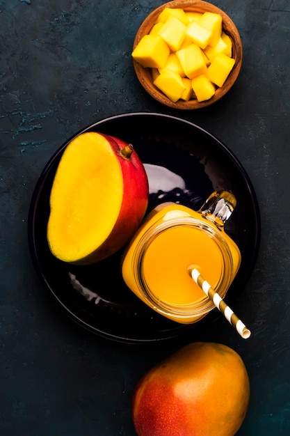 Mango smoothie in glass jar with fresh fruit on blue background copy space top view