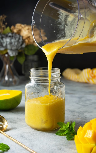 Frullato di mango in barattolo di vetro con frutta fresca di mango e menta, sfondo scuro