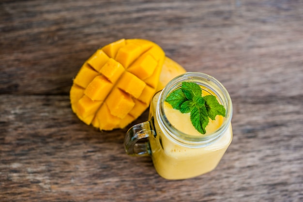 Foto frullato di mango in un barattolo di vetro di vetro e mango sullo sfondo in legno vecchio. frullato di mango.