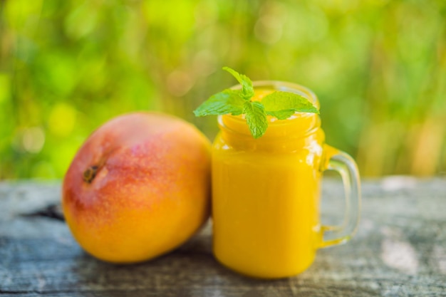Mango smoothie in een glazen Mason pot en mango op de oude houten achtergrond Mango shake Tropisch fruit concept