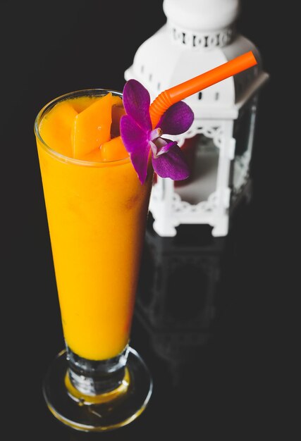 Mango Smoothie in long glass and orchid flower with black background.