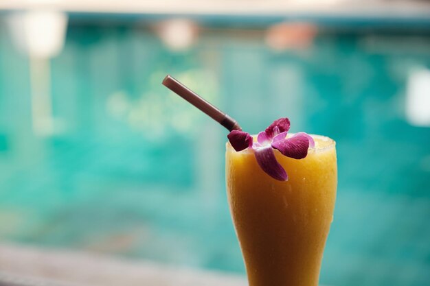 Mango smoothie in a tall glass on the background of the pool