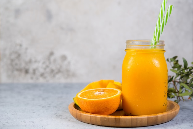 Mango smoothie with orange in a jar and with tubes stands on a gray concrete wall on the right. Clean and healthy food for vegetarians. Healthy diet. Copy space.