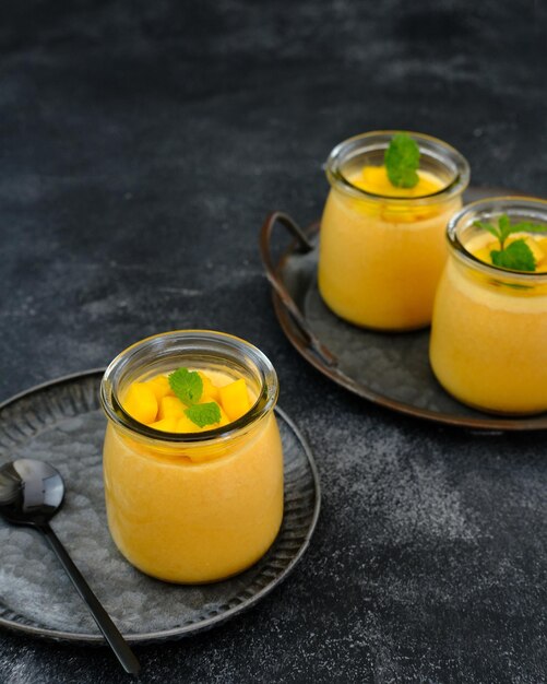 Mangopudding gegarneerd met plakje mango en garnituur van muntblaadjes. Geserveerd in een pot