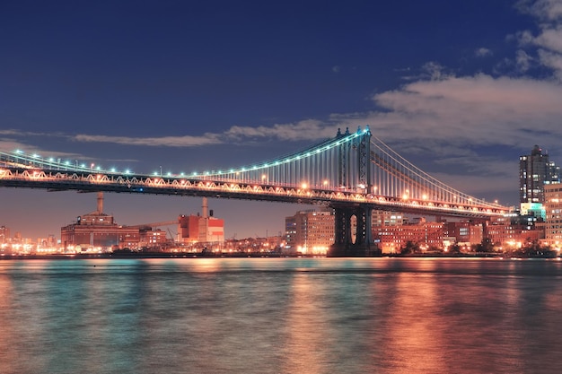 Manhattan Bridge over East River at night in New York City Manhattan with lights and reflections.