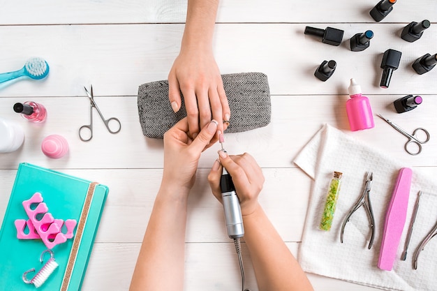 Manicure for the client closeup of the hands of a manicurist and client on a wooden background