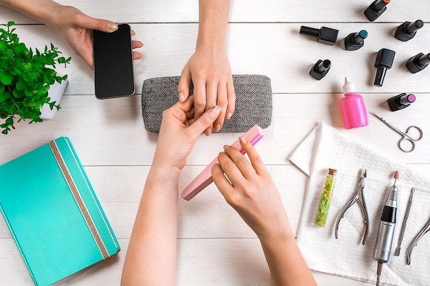 Manicure for the client closeup of the hands of a manicurist and client on a wooden background