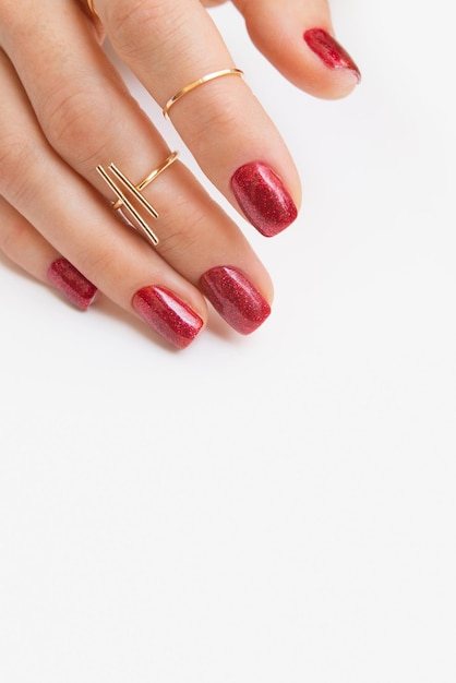 Manicure gel polish of red color with sparkles on female hand with rings Vertical photo with copy space