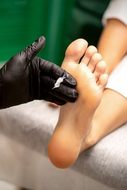 Manicure master applying cream on female client foot massage in\
a beauty salon