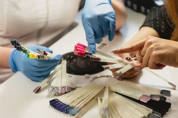 Manicure master in blue rubber gloves helps client in choosing shade nail Polish color. Hands close-up. Professional beauty salon. Hygiene and hand care. Concept of beauty industry