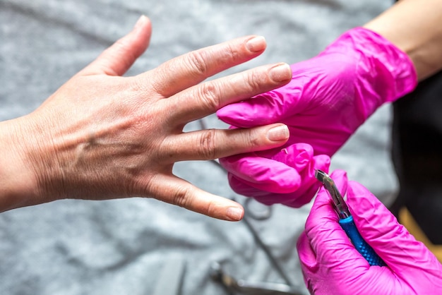 Manicure master in pink gloves scraping off the old coat of varnish in manicure salon using drill Professional manicure in cosmetology clinic Hygiene for feet in beauty salon