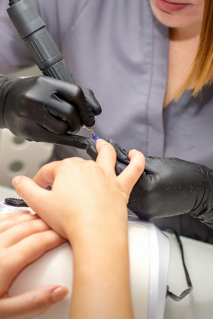 Manicure master in rubber gloves applies an electric nail file to remove the nail polish in a nail salon