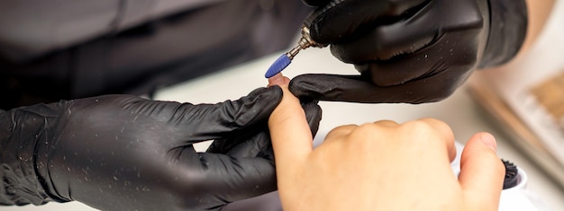 Manicure master uses electric nail file machine in a nail salon close up