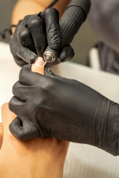 Manicure master uses electric nail file machine in a nail salon close up