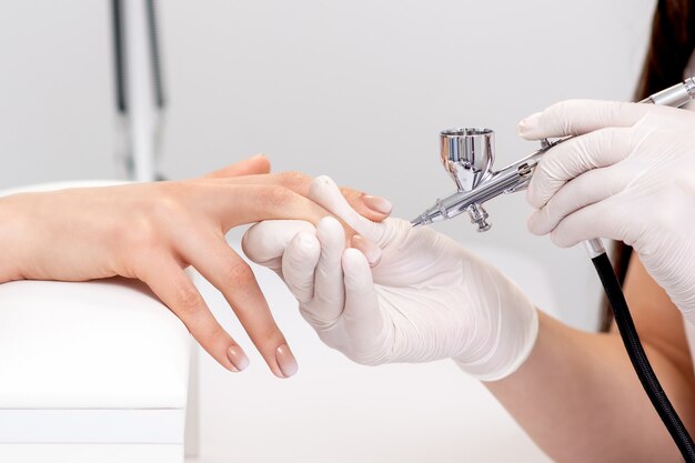 Premium Photo  Young woman receiving manicure by airbrush in nail salon.  procedure for spraying paint on the nails