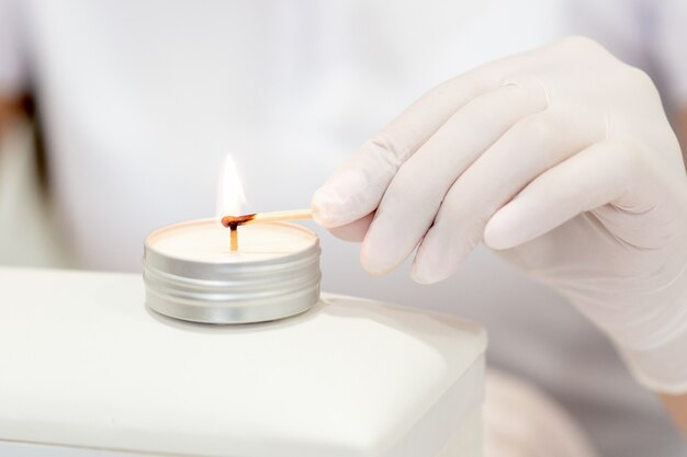 Manicure master in white gloves lighting candle with match in nail salon