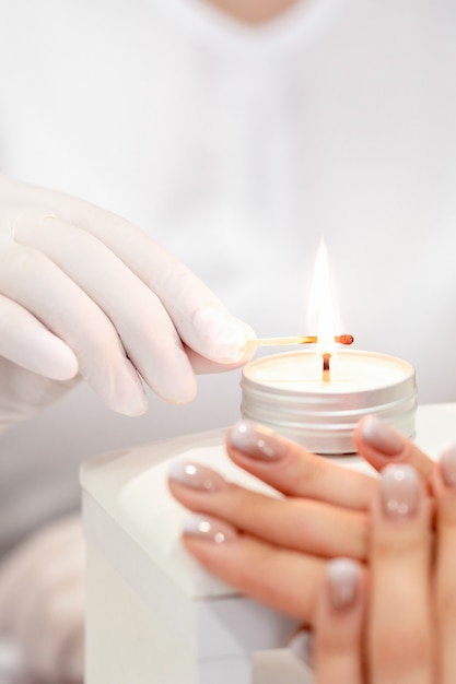 Manicure master in white gloves lighting candle with match in nail salon