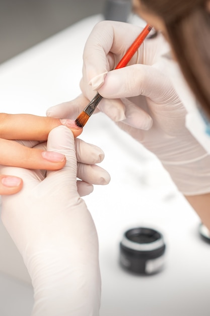 Manicure meester behandelt vrouwelijke nagels met transparante nagellak in een nagelsalon