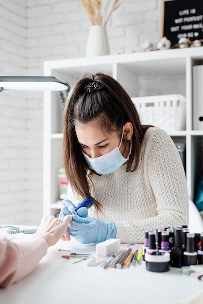 Manicure meester in masker en handschoenen met behulp van een elektrische machine