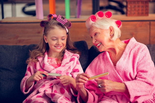 Manicure met oma. Close-up van een meisje dat zich vrolijk voelt terwijl ze manicure doet met oma terwijl ze nagelvijlen gebruikt