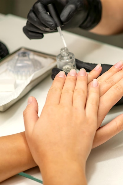 Manicure painting process Manicure master paint the nails with transparent varnish in a nail salon close up