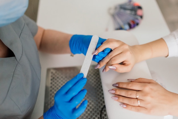 Manicure and pedicure salon, covid-19 and social distance.
master in rubber gloves and young woman client in protective mask
in beauty studio interior.