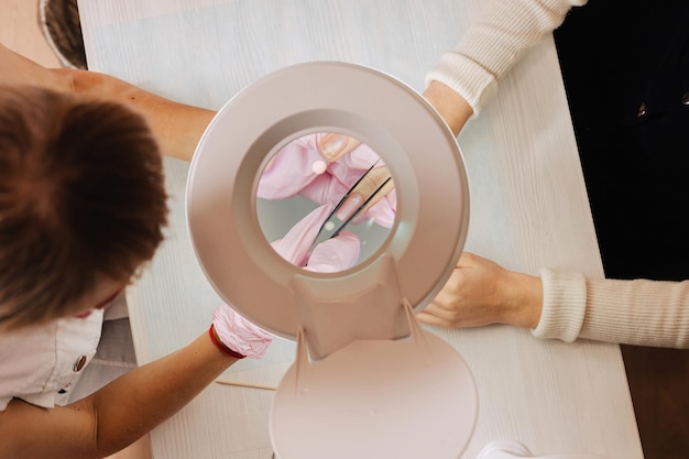 Manicure proces. de meester vormt een kunstnagel van een speciale gel met een pincet. bekijk door een lamp met een vergrootglas.