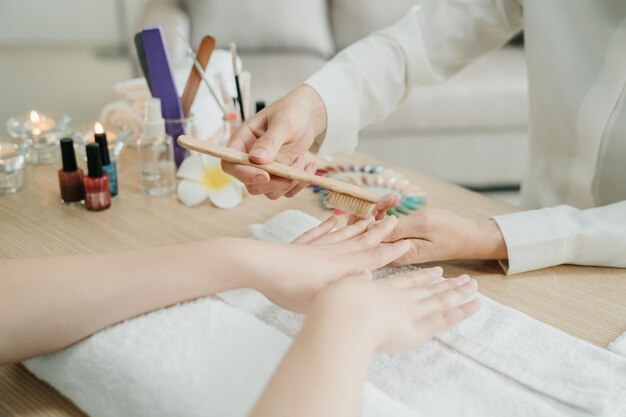 Manicure process at home service. focus on hands of two young asian women worker and customer in living room. Doing manicure nail file by wooden brush to clean up finger on table with candles beside.