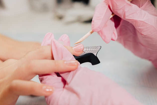 Foto processo di manicure il maestro forma un'unghia artificiale da un gel speciale usando un bastoncino di bambù