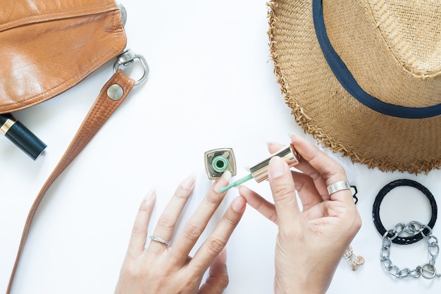 Manicure process. Nail polish being applied to hand, polish is a green color. Woman accessories on white background