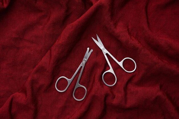 Manicure scissors on red silk background Beauty concept