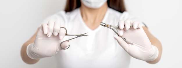 Foto strumenti per manicure nelle mani del manicure femminile che indossa guanti e maschera bianca sul muro bianco