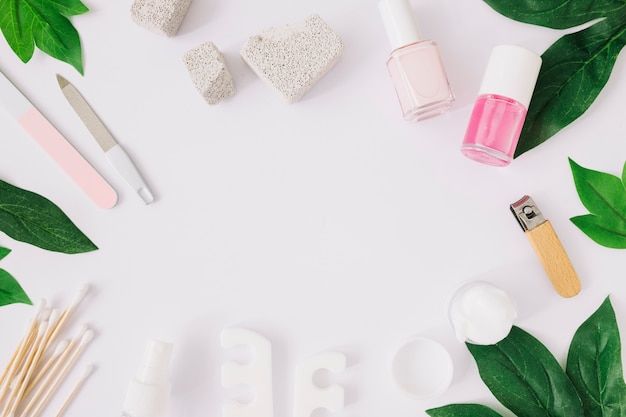 Manicure tools and products with green leaves on white surface