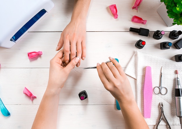 Manicure voor de cliëntclose-up van de handen van een manicure en cliënt op een houten achtergrond