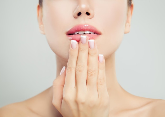 Manicured hand with french manicure and pink glossy lips Woman face macro