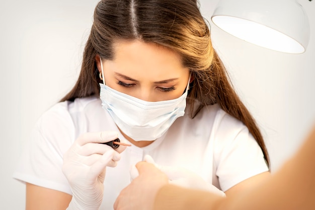 Foto manicuremeester in het witte beschermend masker is nagels lakken