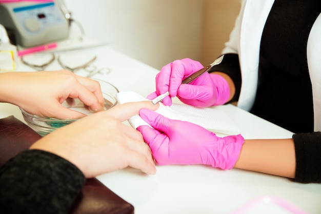 Manicurespecialist in rubberen handschoenen verzorging door vingernagel in spa schoonheidssalon. Manicure gebruikt professionele manicure tool. Manicureservice.