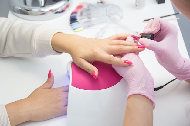 Manicurist apply nail Polish. Close-up of a woman applying nail Polish to her finger nails.Pink nails.