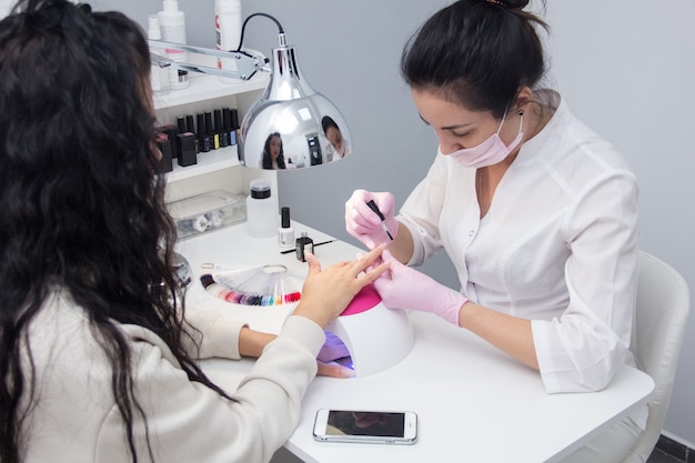 The manicurist covers her nails with nail Polish. A woman does a manicure and applies nail Polish