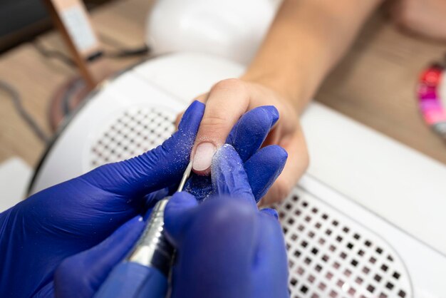 Foto la manicure taglia le cuticole delle unghie con una fresatrice elettrica indossando guanti di lattice blu